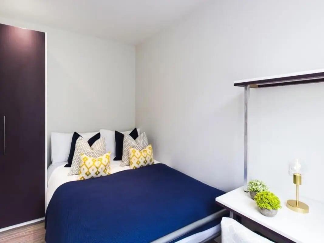 Dark wardrobe blue bed patterned pillows desk lamp bedroom at 2 Queen Anne Street in Stoke-On-Trent Student Accommodation