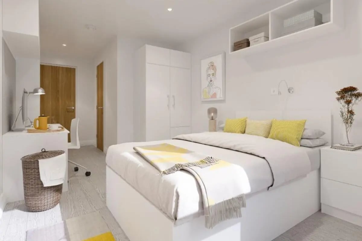 Bed with yellow pillows desk and hamper bedroom at The Reservoir in Plymouth Student Accommodation