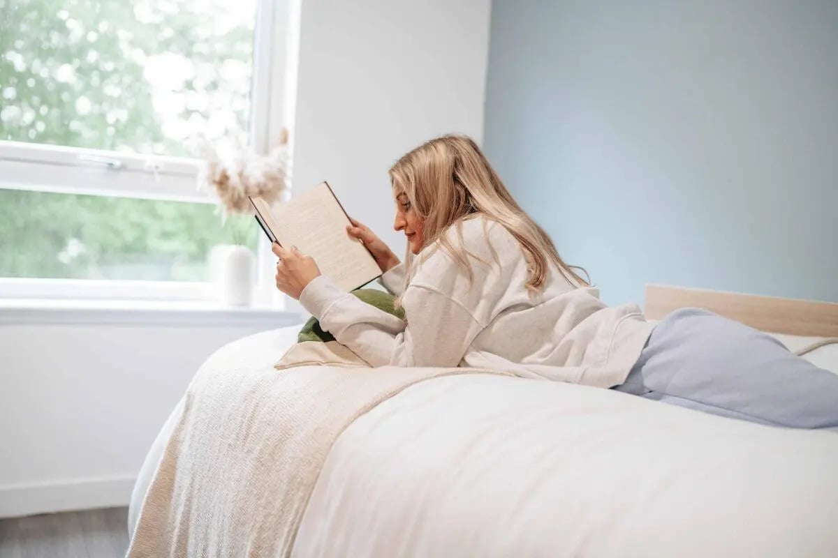 Woman reading on bed with window and vase bedroom at Caledon Court in Aberdeen Student Accommodation