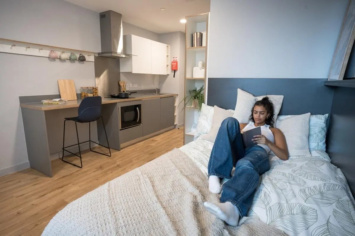 Woman reading on bed kitchen area study area bedroom at West Wing in Cardiff Student Accommodation