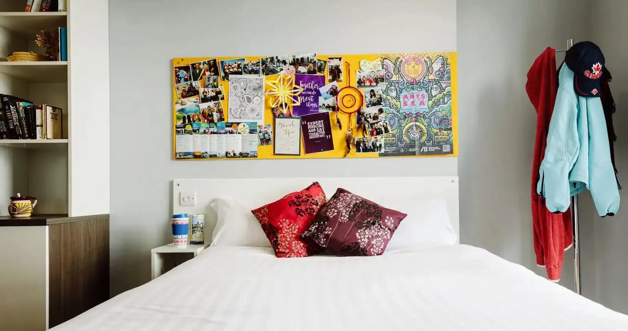 Bed with pillows noticeboard and coats bedroom at Kaplan Living Bournemouth in Bournemouth Student Accommodation