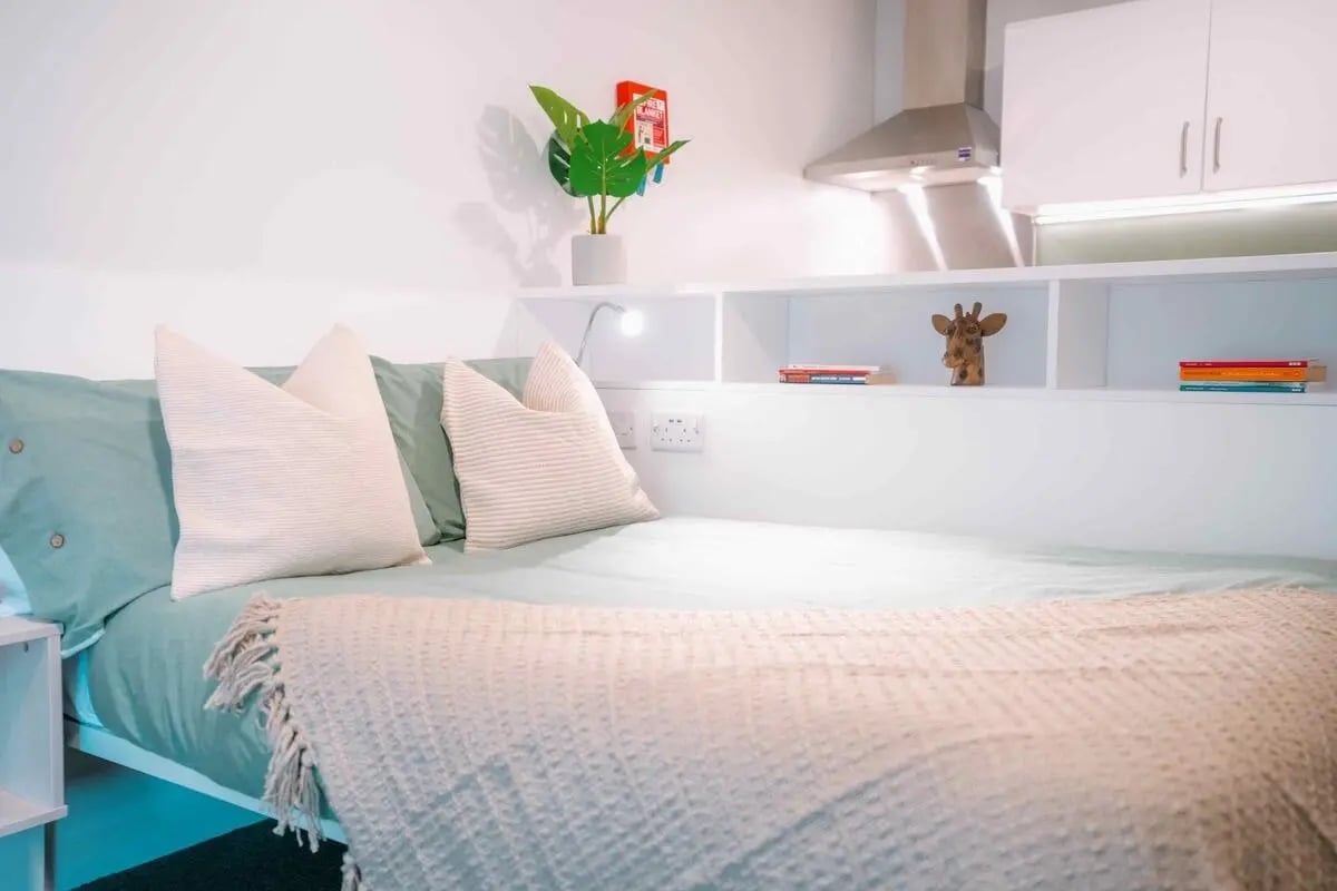 Bed pillows throw plant bookshelf kitchen hood bedroom at Base in Glasgow Student Accommodation