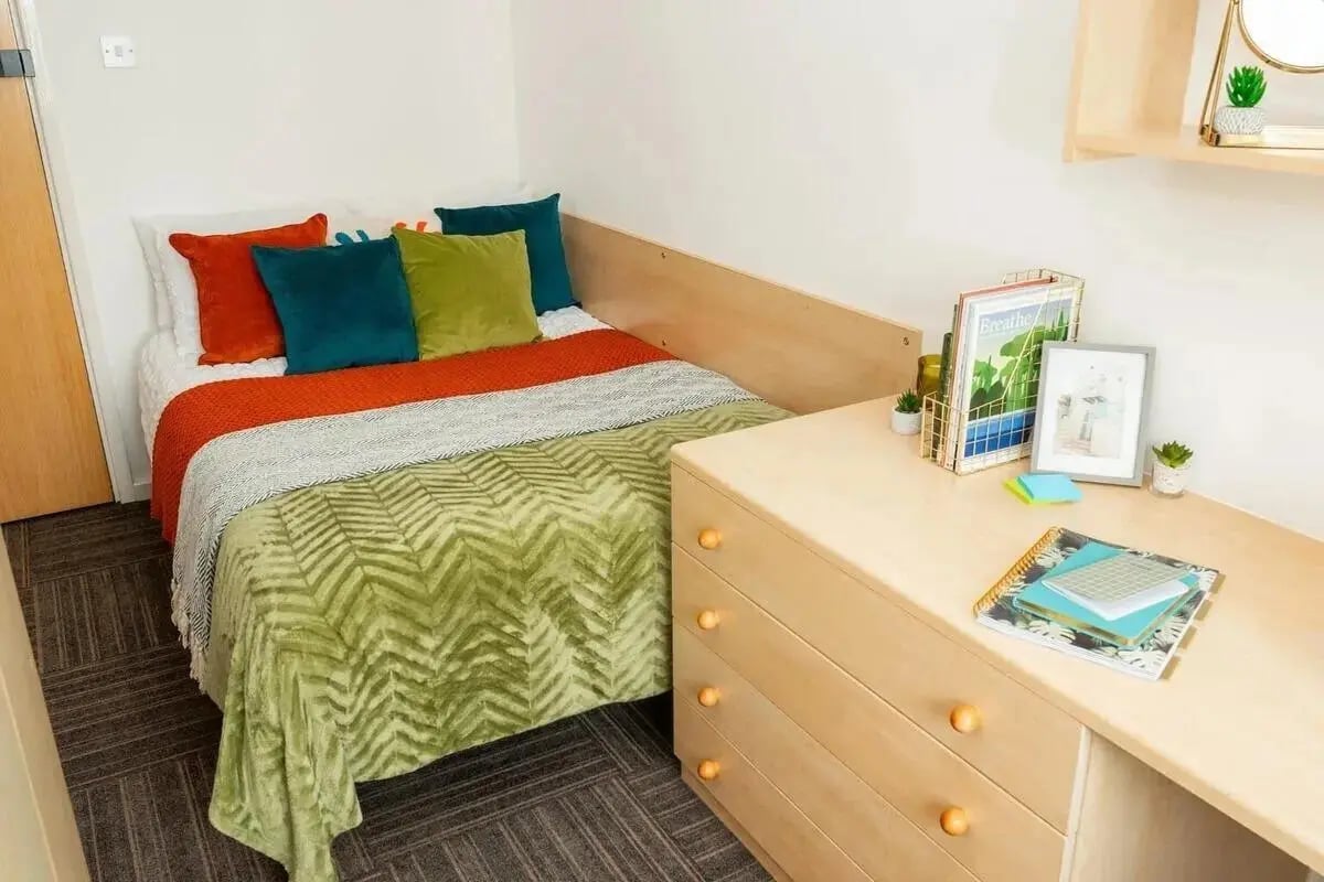 Bed with colorful pillows and desk with notebooks bedroom at Marybone Student Village 1 in Liverpool Student Accommodation