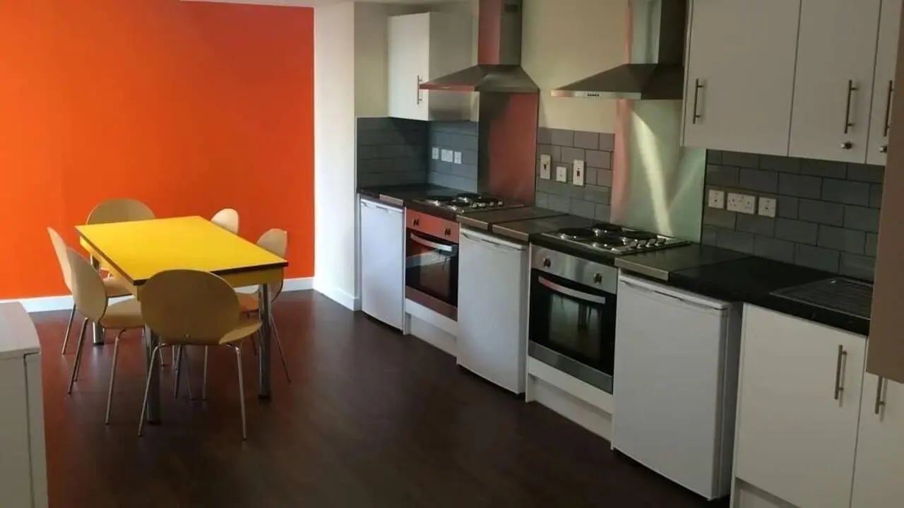 Orange wall yellow table chairs kitchen with ovens and fridges at Alliance House in London Student Accommodation