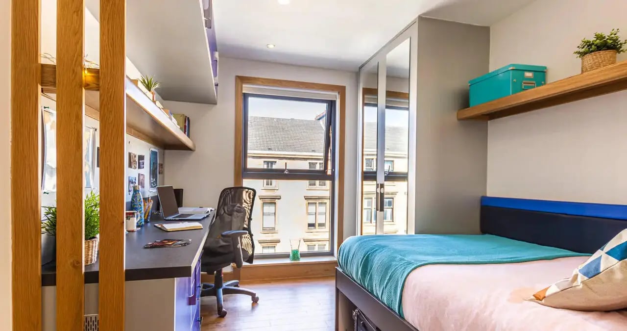 Desk with laptop bed with blue accent bedroom at Kaplan Living Glasgow - Argyle Street in Glasgow Student Accommodation