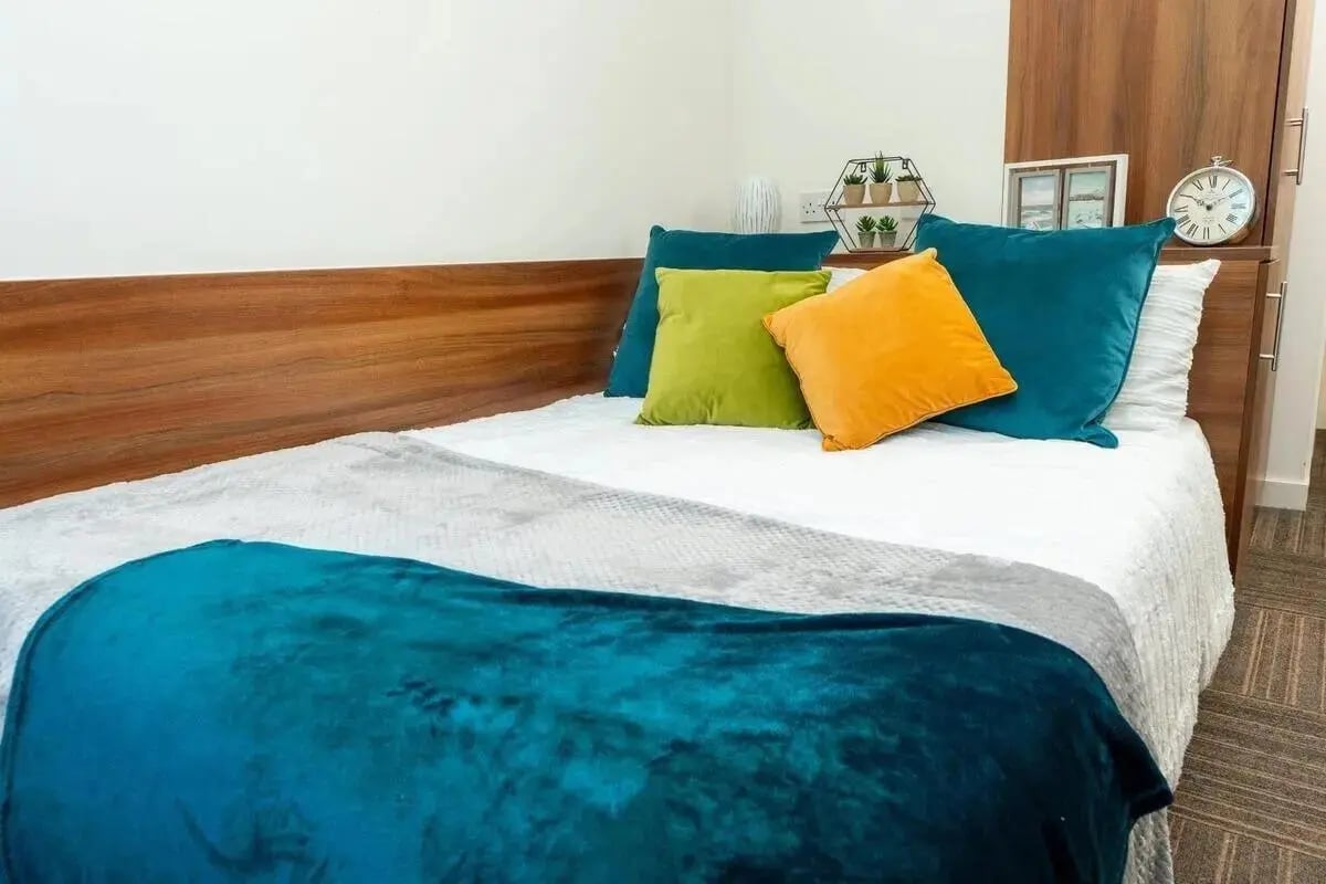 Bed with teal orange green pillows and throws bedroom at Denmark Road in Manchester Student Accommodation