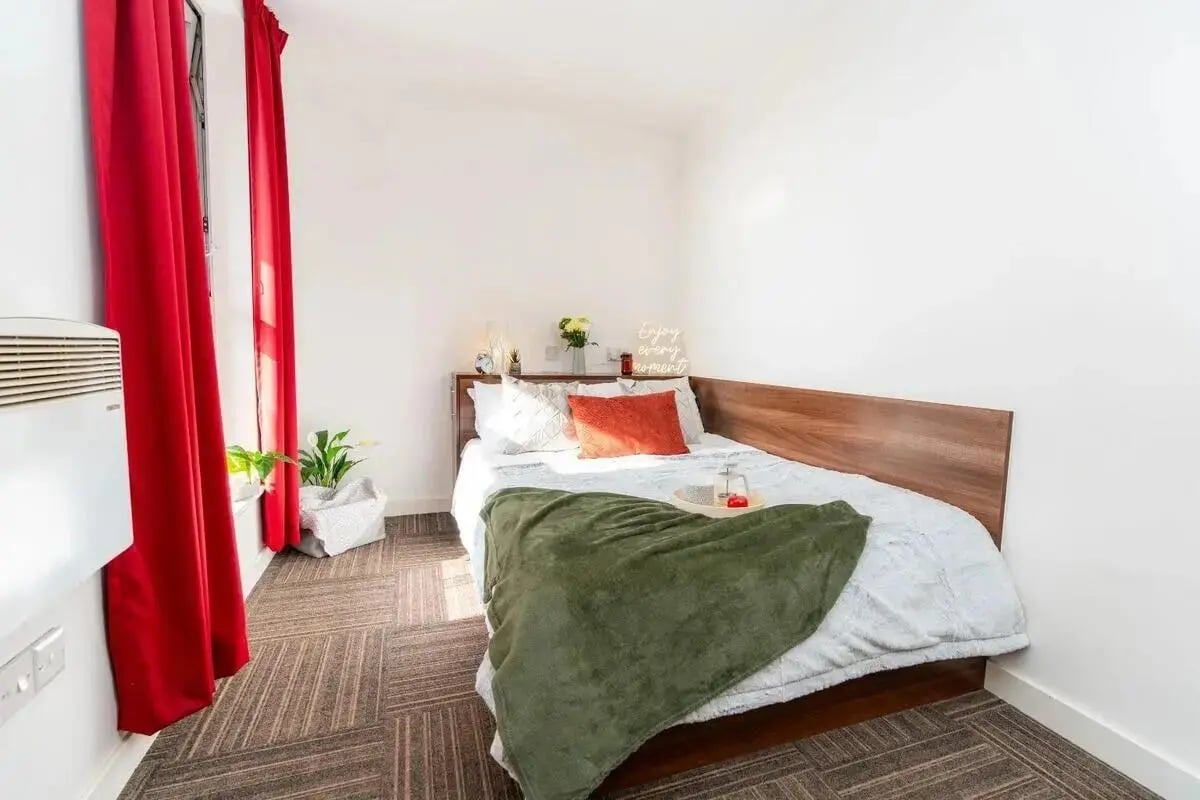Bed with green blanket and red pillows bedroom at Denmark Road in Manchester Student Accommodation