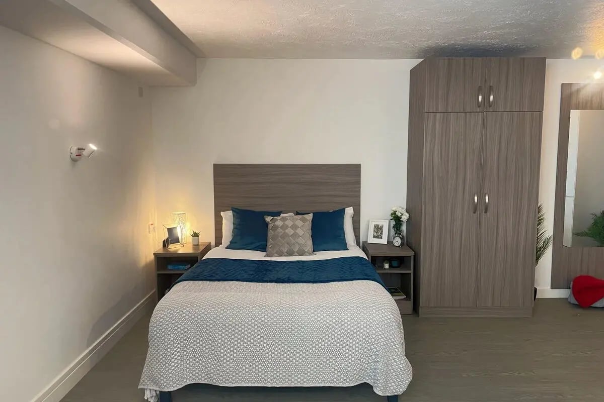 Bed with blue pillows wardrobe beside it bedroom at Manna Ash House in London Student Accommodation