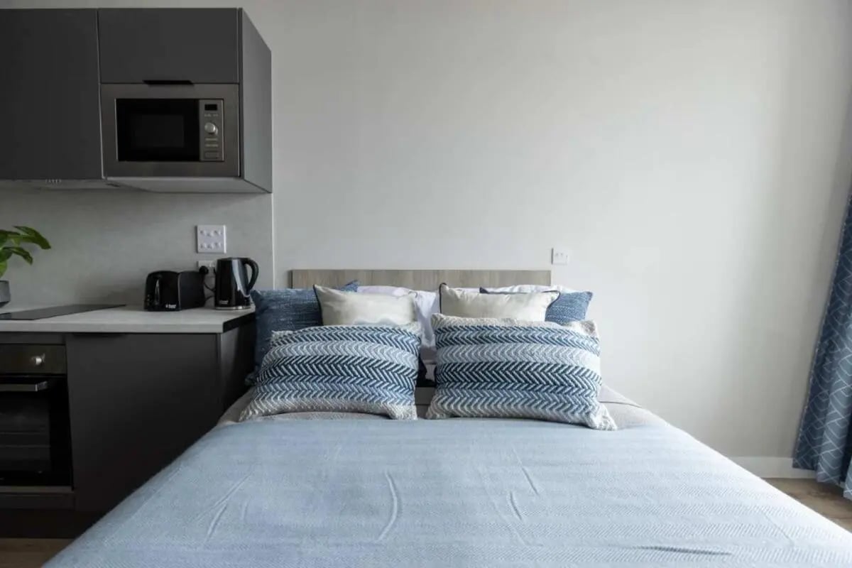 Bed with blue patterned pillows microwave and kettle bedroom at Boutique Student Living Swansea in Swansea Student Accommodation
