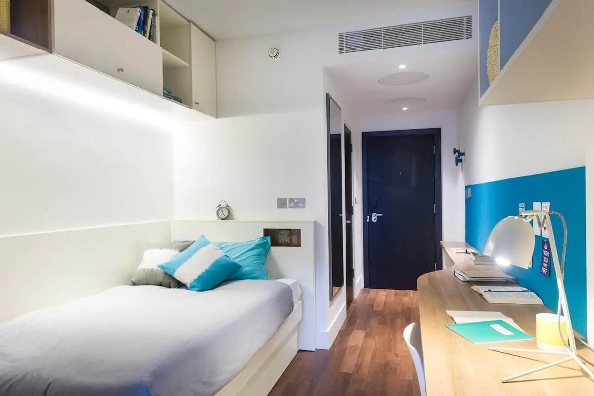 Bed with pillows desk with lamp and blue wall bedroom at Spring Mews in London Student Accommodation