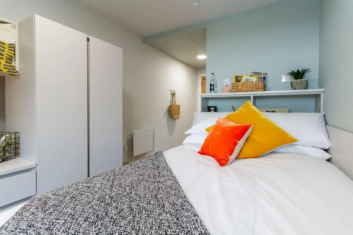 Bed with orange yellow pillows white bedding Bedroom at The Refinery in Leeds Student Accommodation