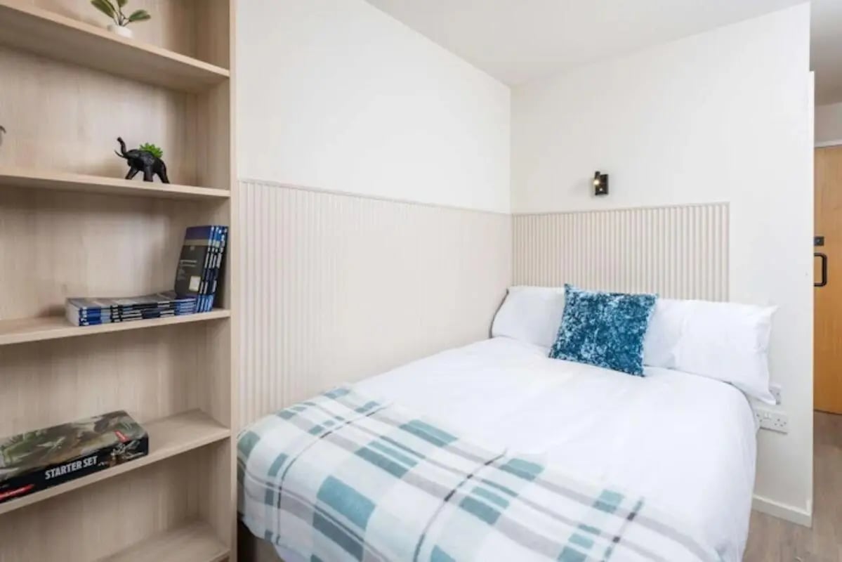 Bed with blue pillow and plaid blanket bookshelf Bedroom at The Railyard in Liverpool Student Accommodation