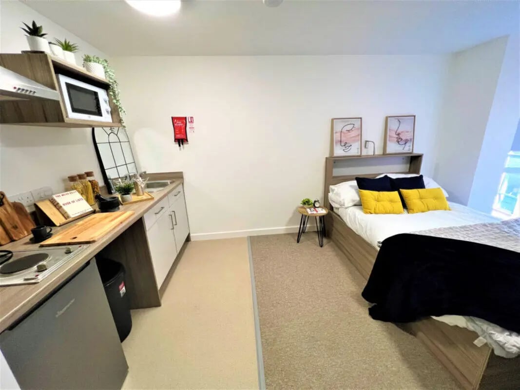 Kitchenette and bed with yellow pillows Bedroom at Q Studios in Stoke-On-Trent Student Accommodation