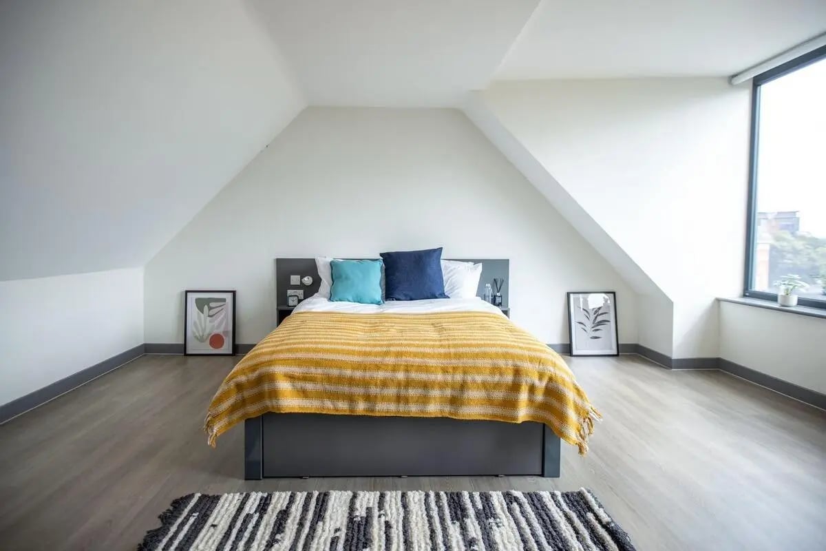 Bed with yellow blanket blue pillows artwork and rug bedroom at Canvas Capital House in Southampton Student Accommodation