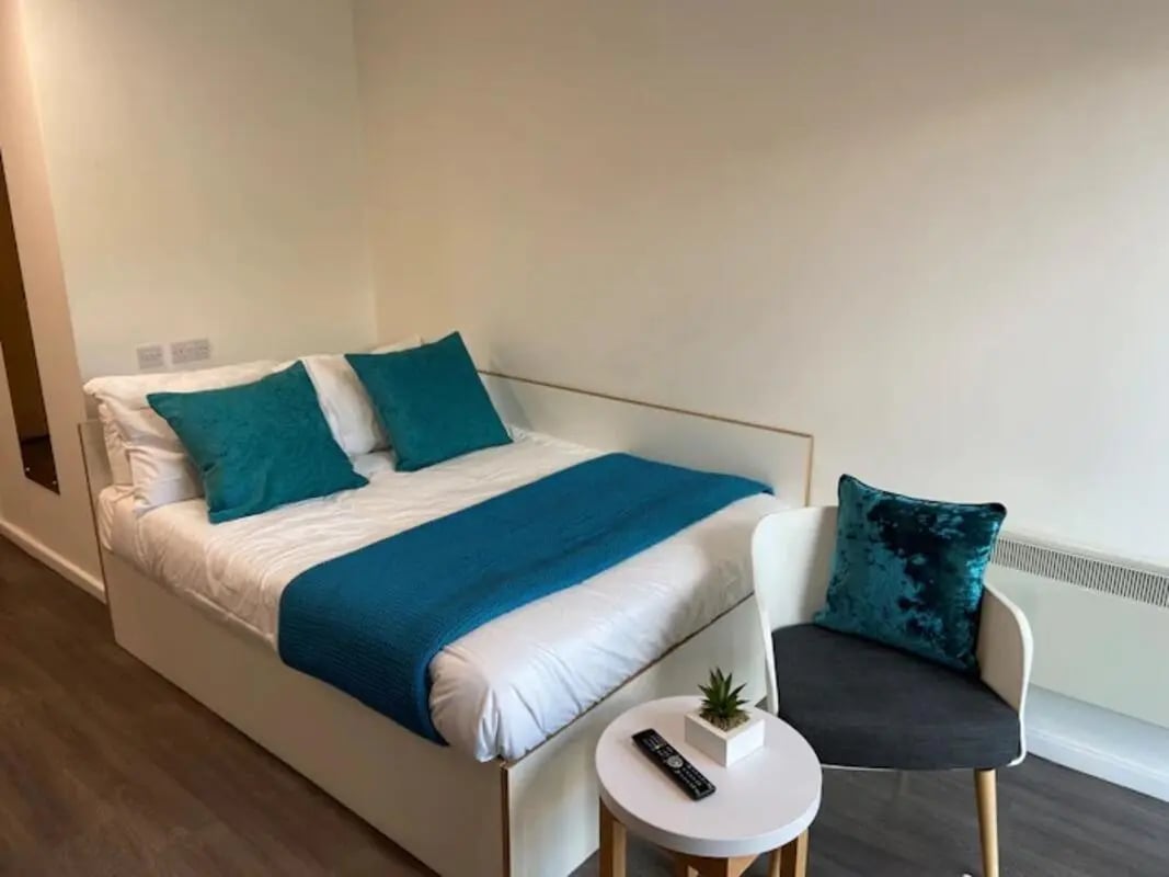 Bed with teal cushions and throw beside chair bedroom at Laycock Studios in Sheffield Student Accommodation
