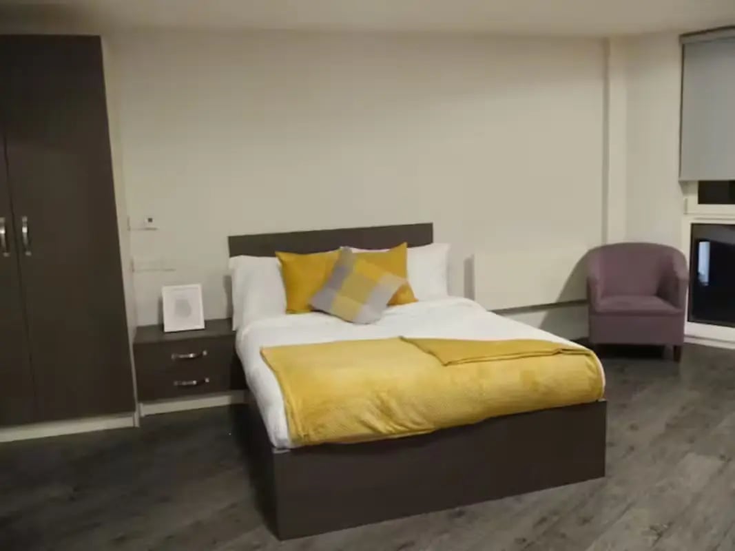 Bed with yellow blankets beside wardrobe and armchair bedroom at Cornerhouse in Sheffield Student Accommodation