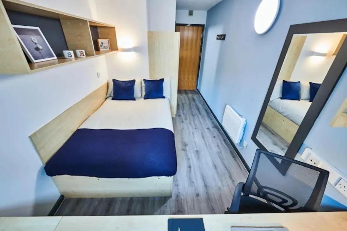 Bed with blue pillows large mirror chair bedroom at Capital Gate in Liverpool Student Accommodation