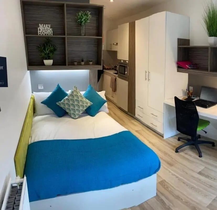 Bed with blue pillows and kitchen study area bedroom at Newcastle 1 in Newcastle Upon Tyne Student Accommodation