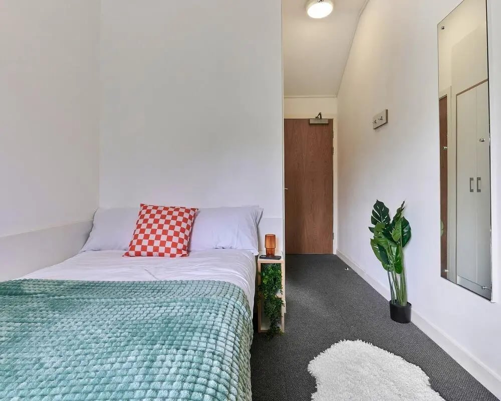 Bed with mint blanket and red pillow bedroom at The Village at The Viaduct in Durham Student Accommodation