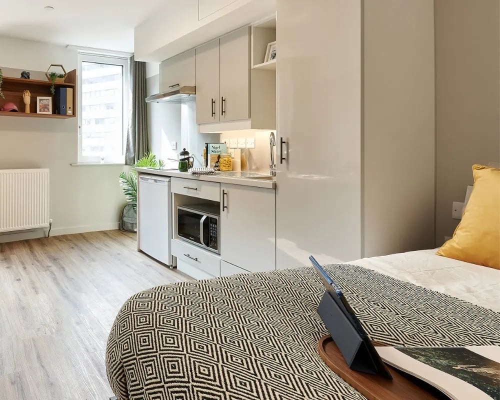 Bed with patterned blanket kitchen unit radiator window studio flat at The Helix in London Student Accommodation