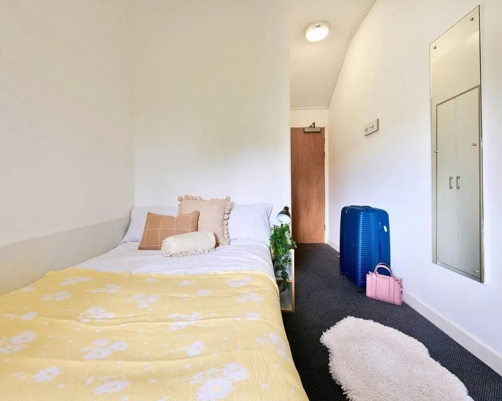Bed with yellow blanket luggage mirror bedroom at The Village at The Viaduct in Durham Student Accommodation