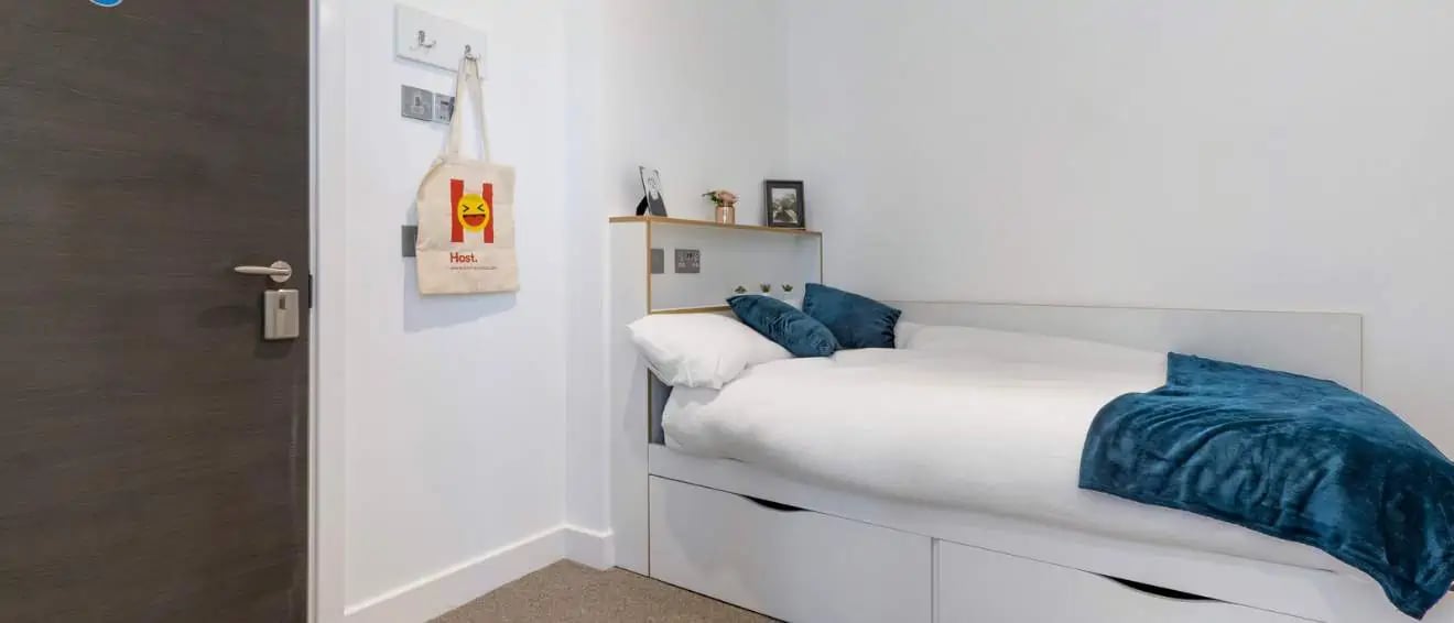 Bed with teal throw blue pillows and tote bag bedroom at 27 Magdalen Street in Colchester Student Accommodation