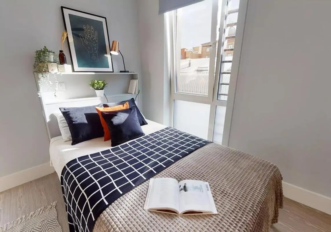 Bed with pillows artwork and open book bedroom at iQ Magenta House in London Student Accommodation