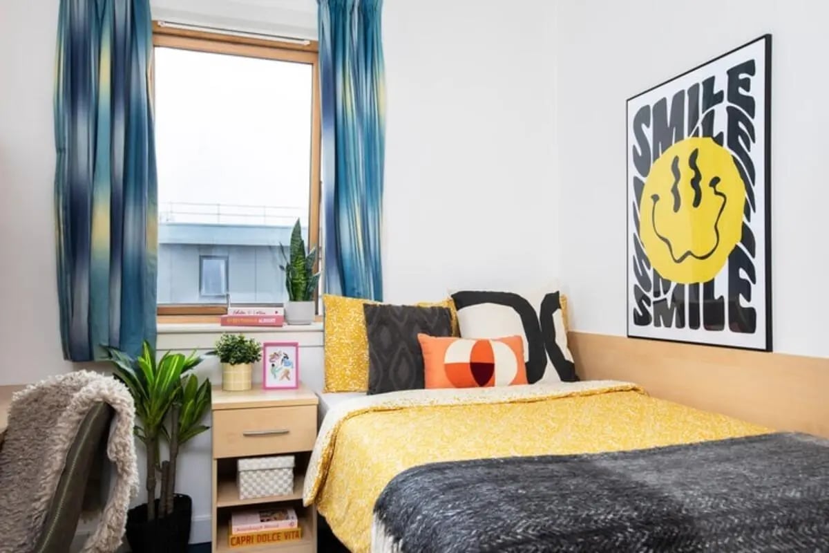 Bed with yellow blanket pillows and smiley poster bedroom at Pier Quays in Medway Student Accommodation