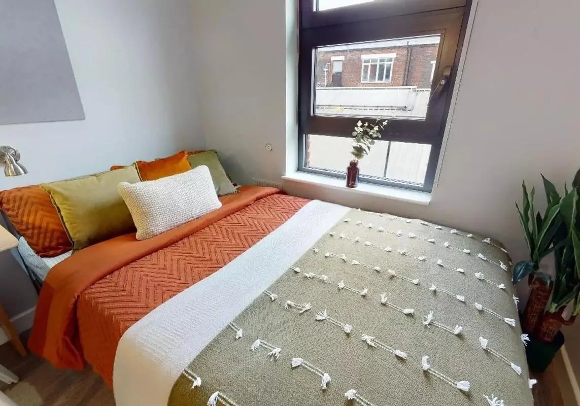 Bed with orange and green throws and pillows bedroom at iQ Steel in Sheffield Student Accommodation