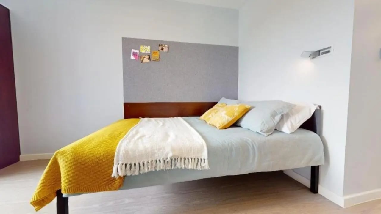 Bed with yellow blanket and bulletin board bedroom at iQ Highbury in London Student Accommodation