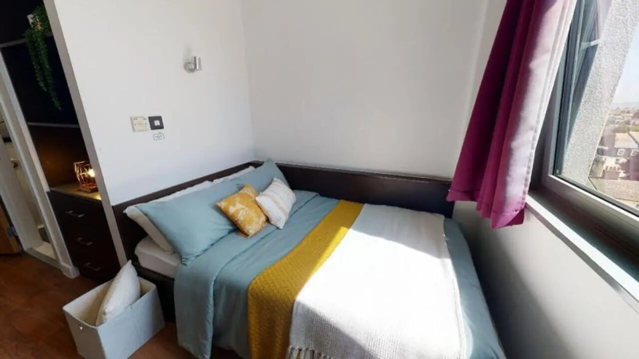Bed with blue bedding yellow accent pillows bedroom at iQ Astor House in Plymouth Student Accommodation