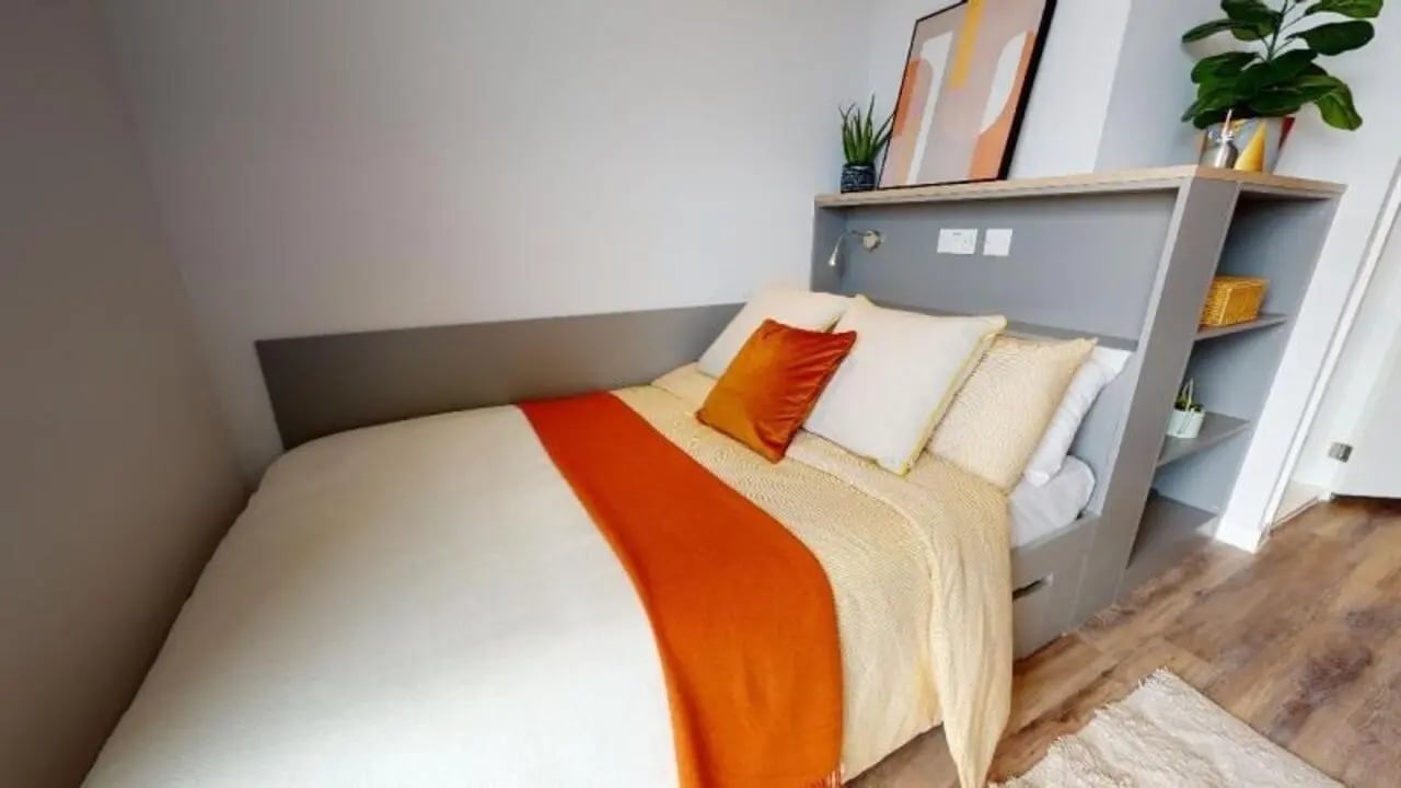 Bed with orange throw and pillows bedroom at iQ Altus House in Leeds Student Accommodation