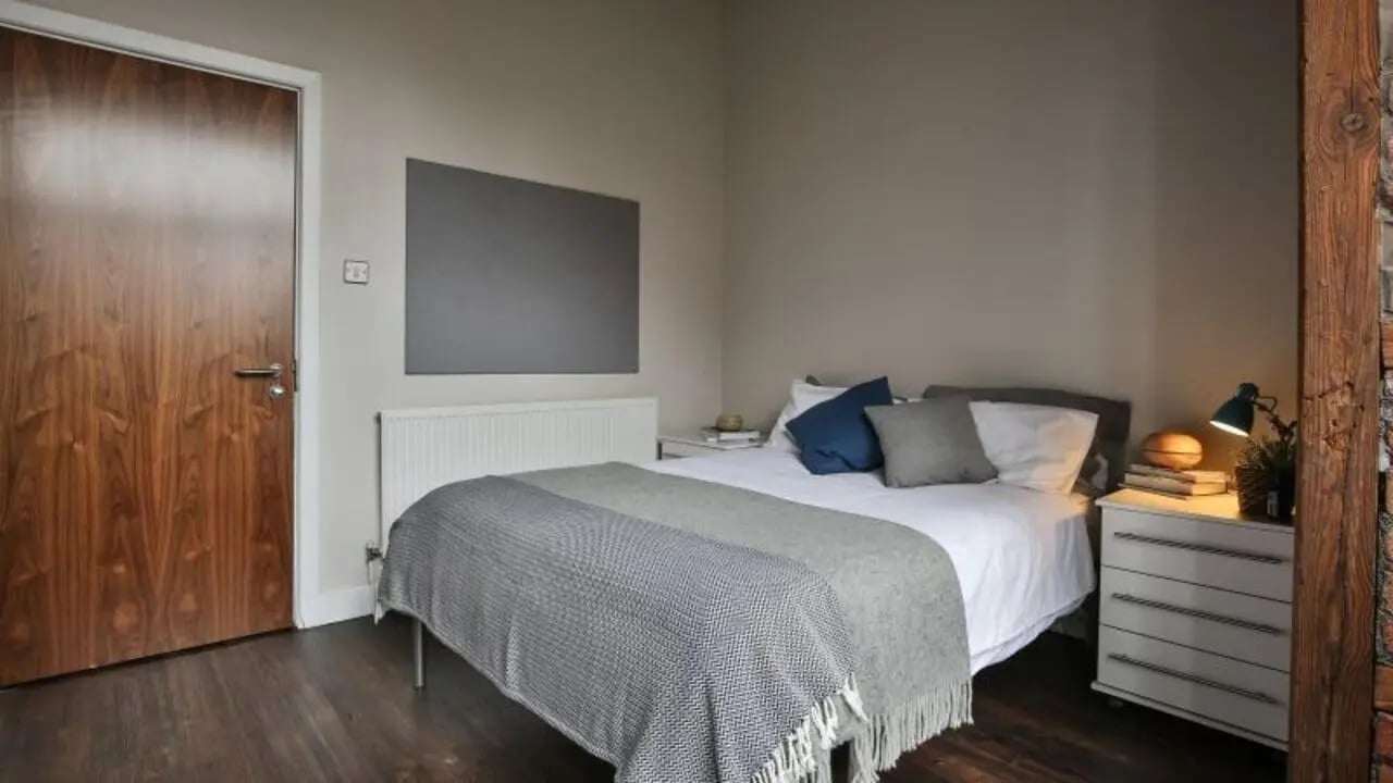 Bed with grey throws and wooden door bedroom at iQ Hollingworth House in Manchester Student Accommodation