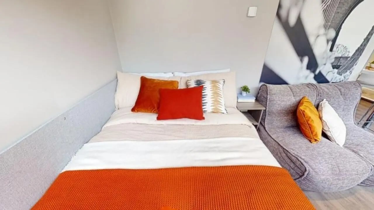Bed with orange and red pillows grey sofa bedroom at Waterlane House in Bristol Student Accommodation