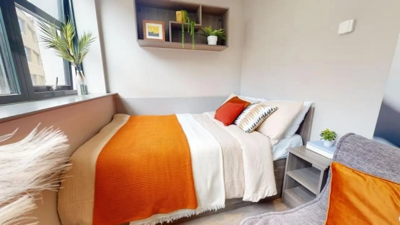 Bed with orange throw pillows and shelf bedroom at Waterlane House in Bristol Student Accommodation