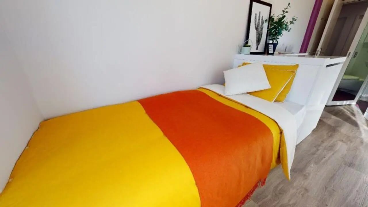 Bed with orange yellow blanket pillows bedroom at iQ East Court in London Student Accommodation