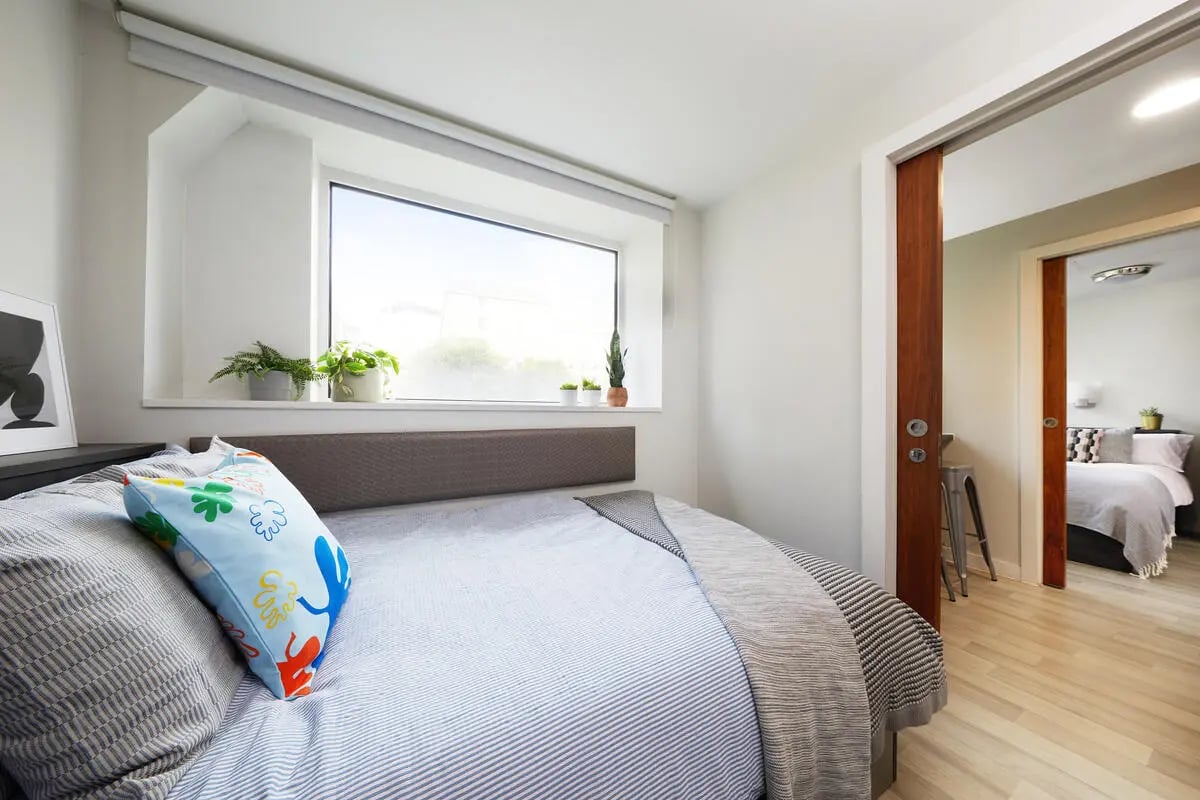 Bed with patterned pillow window plants bedroom at Collegiate Tower in Bristol Student Accommodation