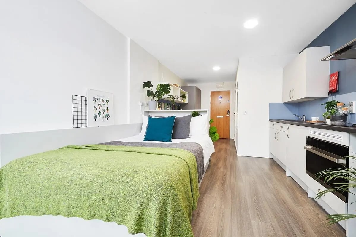 Bed with green blanket and kitchen area studio at Granary Studios in Chester Student Accommodation