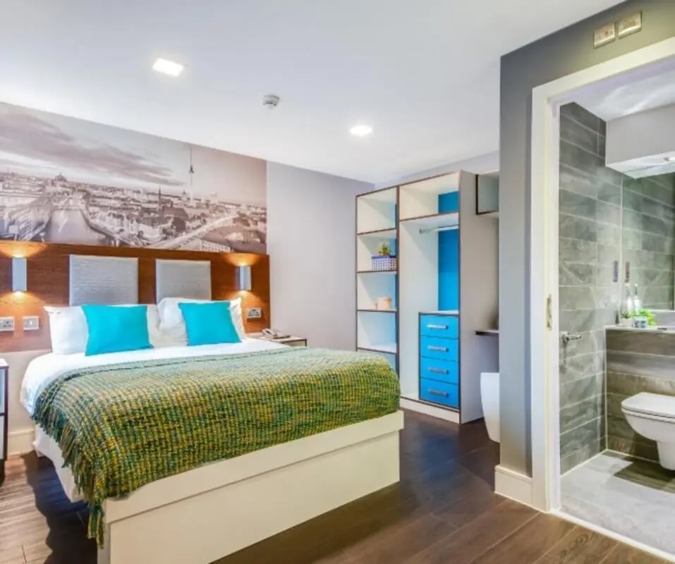 Bed with blue pillows large mural wardrobe and bathroom bedroom at The Edge - Leeds in Leeds Student Accommodation