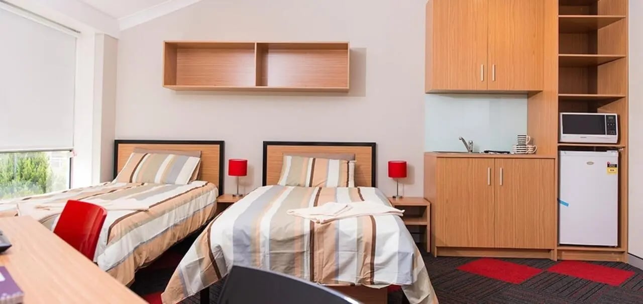 Two beds with striped bedding and red lamps bedroom kitchen area at Sydney Student Living Concord in Sydney Student Accommodation