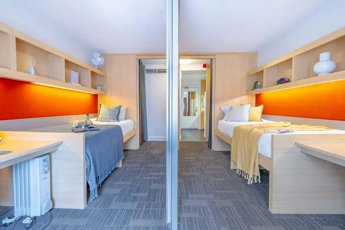 Two beds desks shelves fan in shared bedroom at dwell Village Melbourne City in Melbourne Student Accommodation