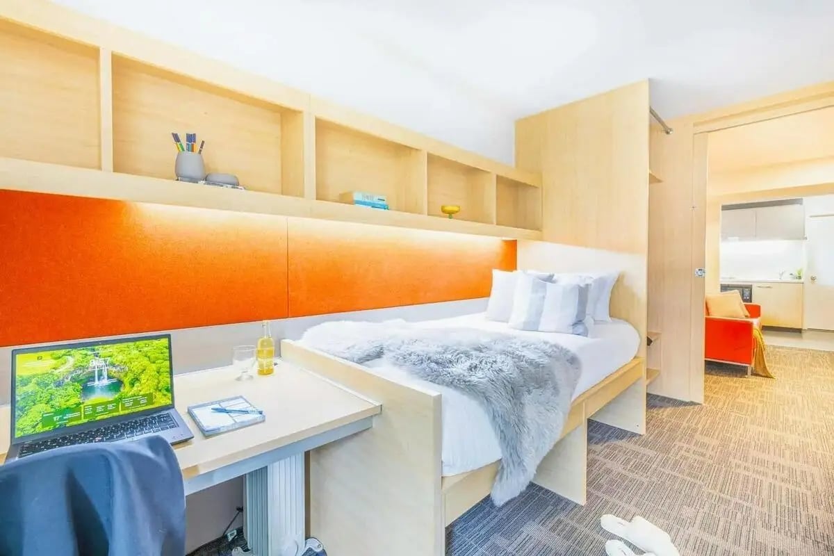 Bed desk shelves laptop and orange accent bedroom at dwell Village Melbourne City in Melbourne Student Accommodation
