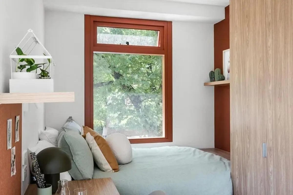 Bed with pillows window lamp and plants bedroom at Campus House in Melbourne Student Accommodation