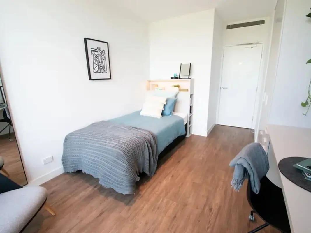 Single bed with blue bedding and grey throw bedroom at Yugo Berkeley Street in Melbourne Student Accommodation