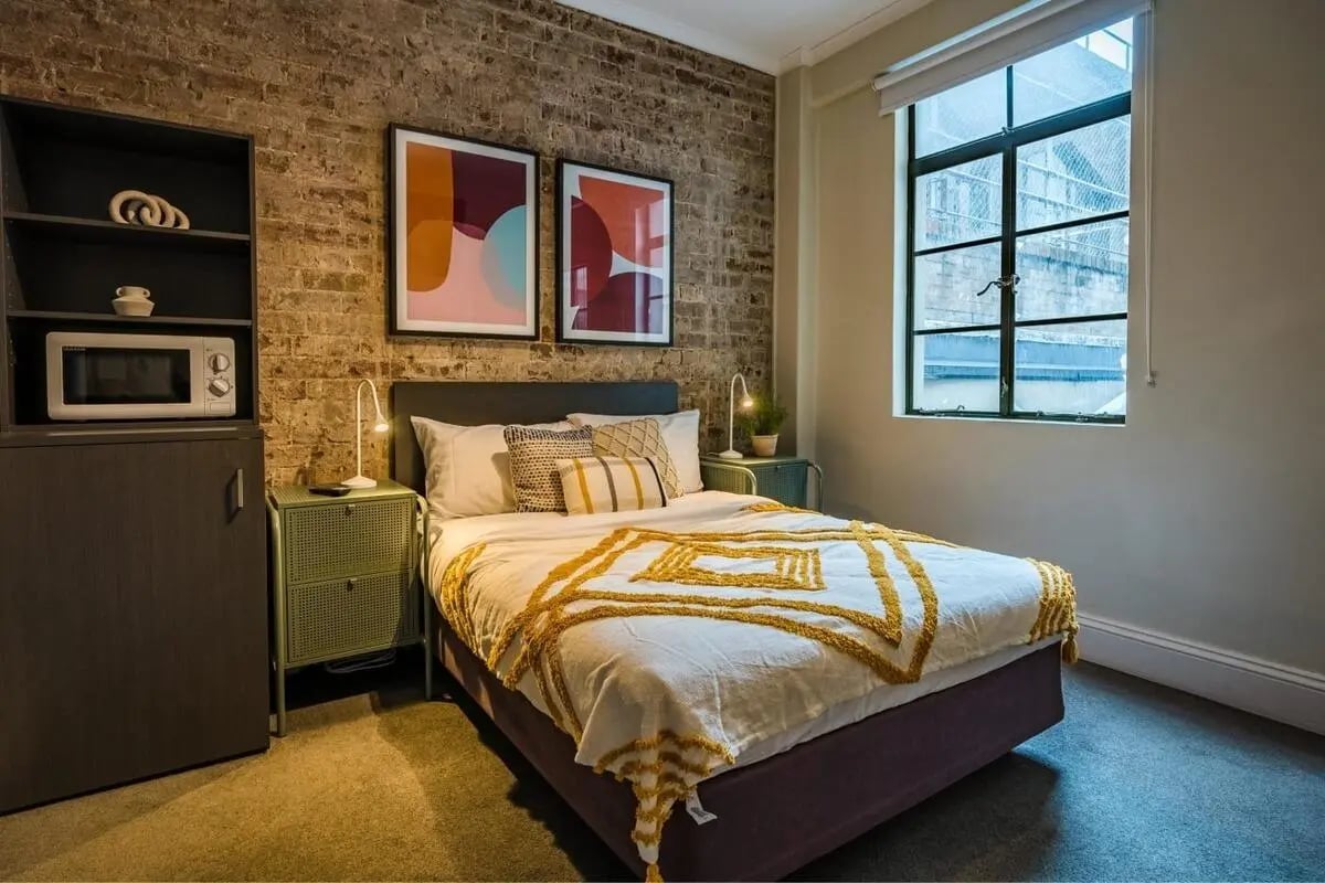 Bed with yellow throw microwave and art Bedroom Image at ume Haymarket in Sydney Student Accommodation