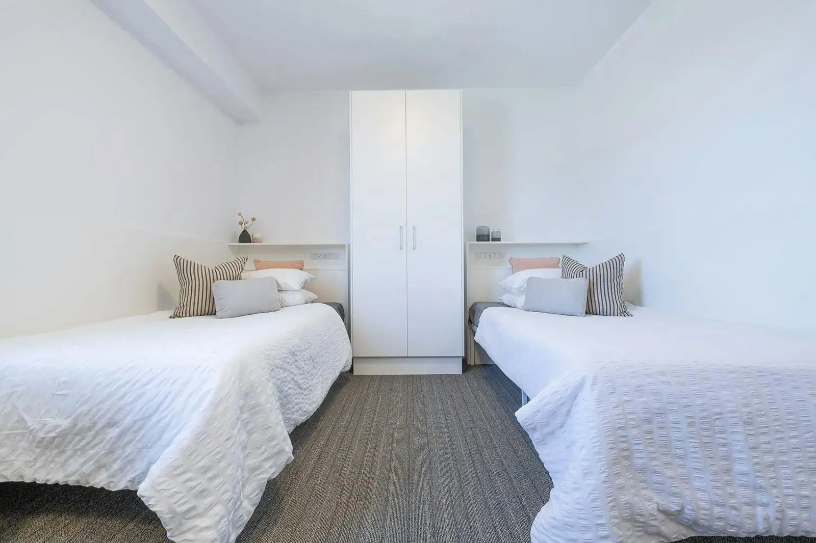 Two beds wardrobe white bedding pillows bedroom at dwell East End Adelaide in Adelaide Student Accommodation