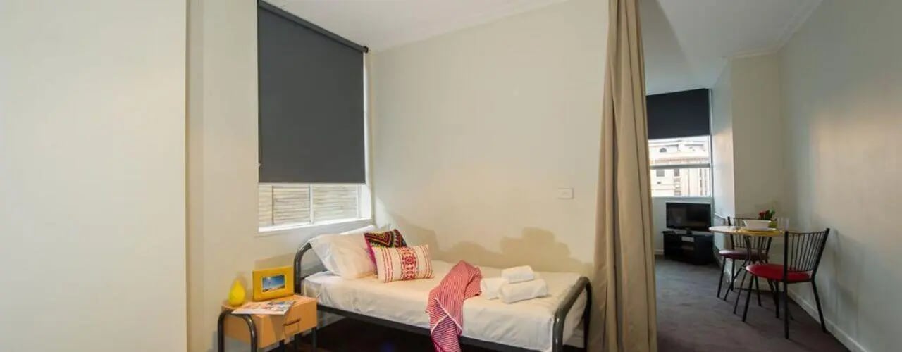 Bed with pillows and table with chairs Studio at Student Living-339 Swanston in Melbourne Student Accommodation