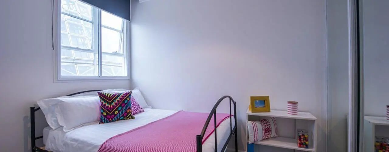 Bed with pink blanket colorful pillows bedside shelf bedroom at Student Living-339 Swanston in Melbourne Student Accommodation