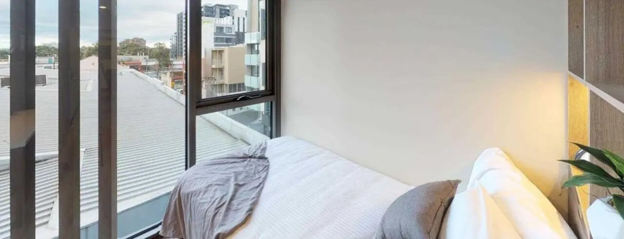Bed with grey throw pillows and plant bedroom at UniLodge Royal Melbourne in Melbourne Student Accommodation