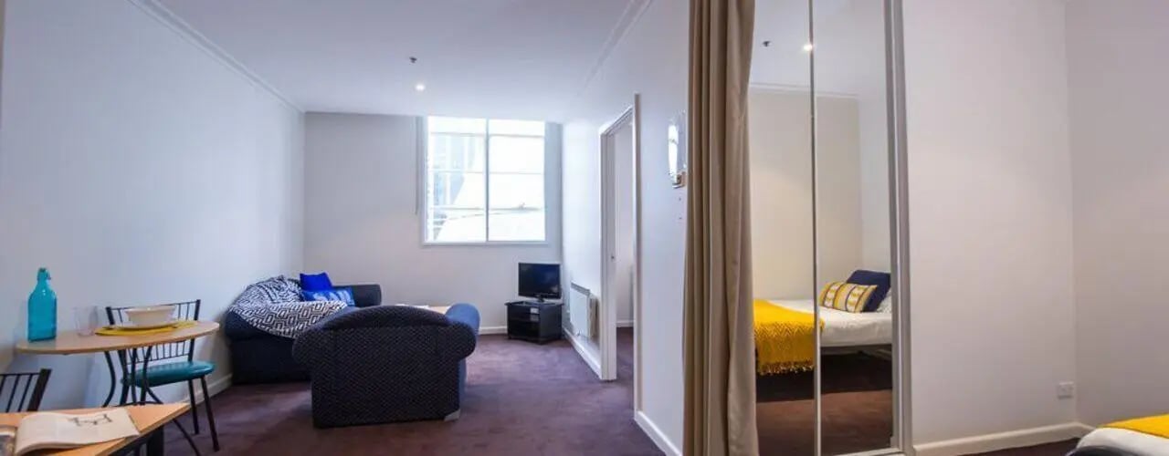 Sofa table chairs TV bed with yellow blanket Living room at Student Living-339 Swanston in Melbourne Student Accommodation